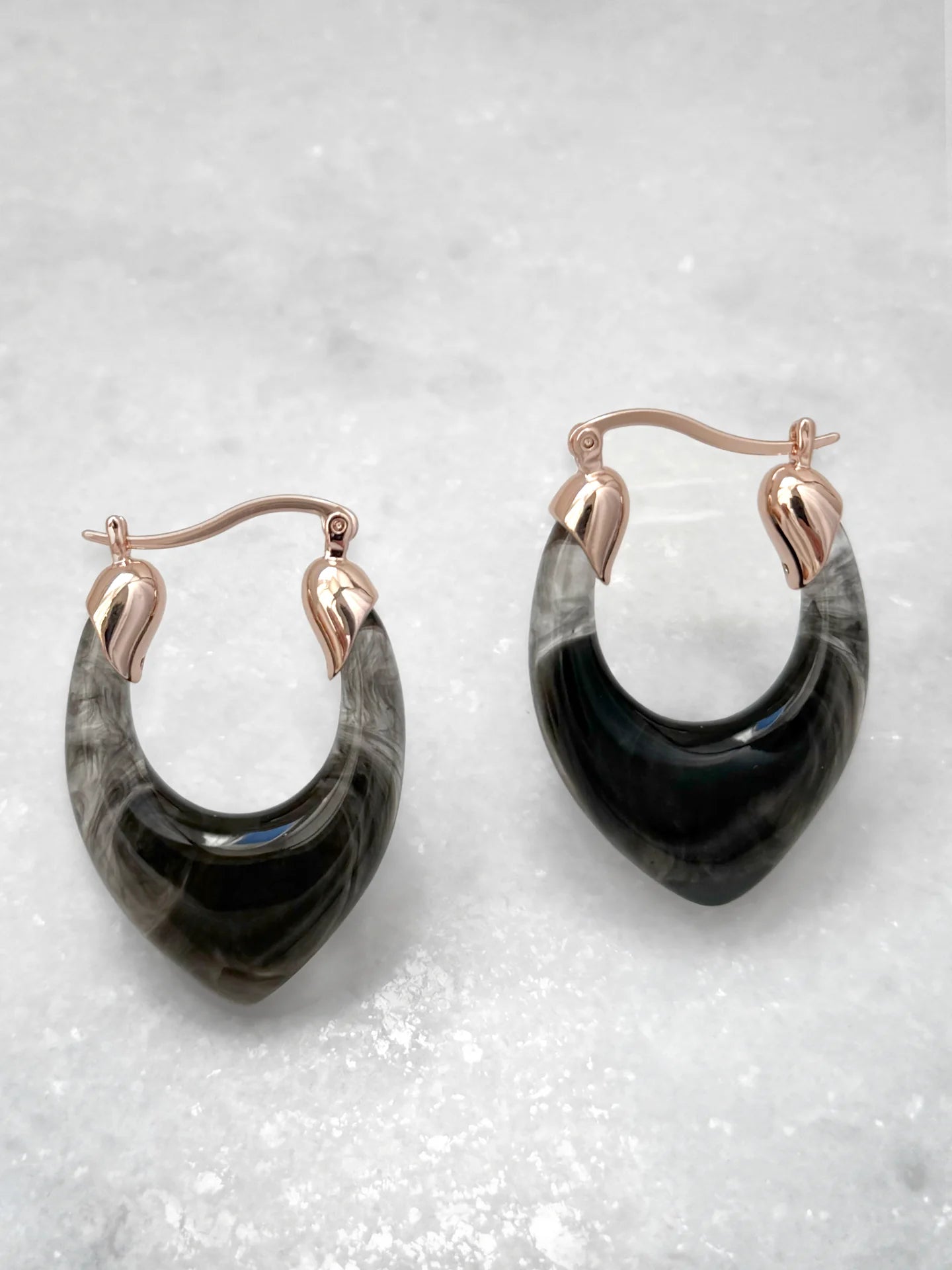 Pair of teardrop hoop earrings with marbled black resin and gold metal accents on white background