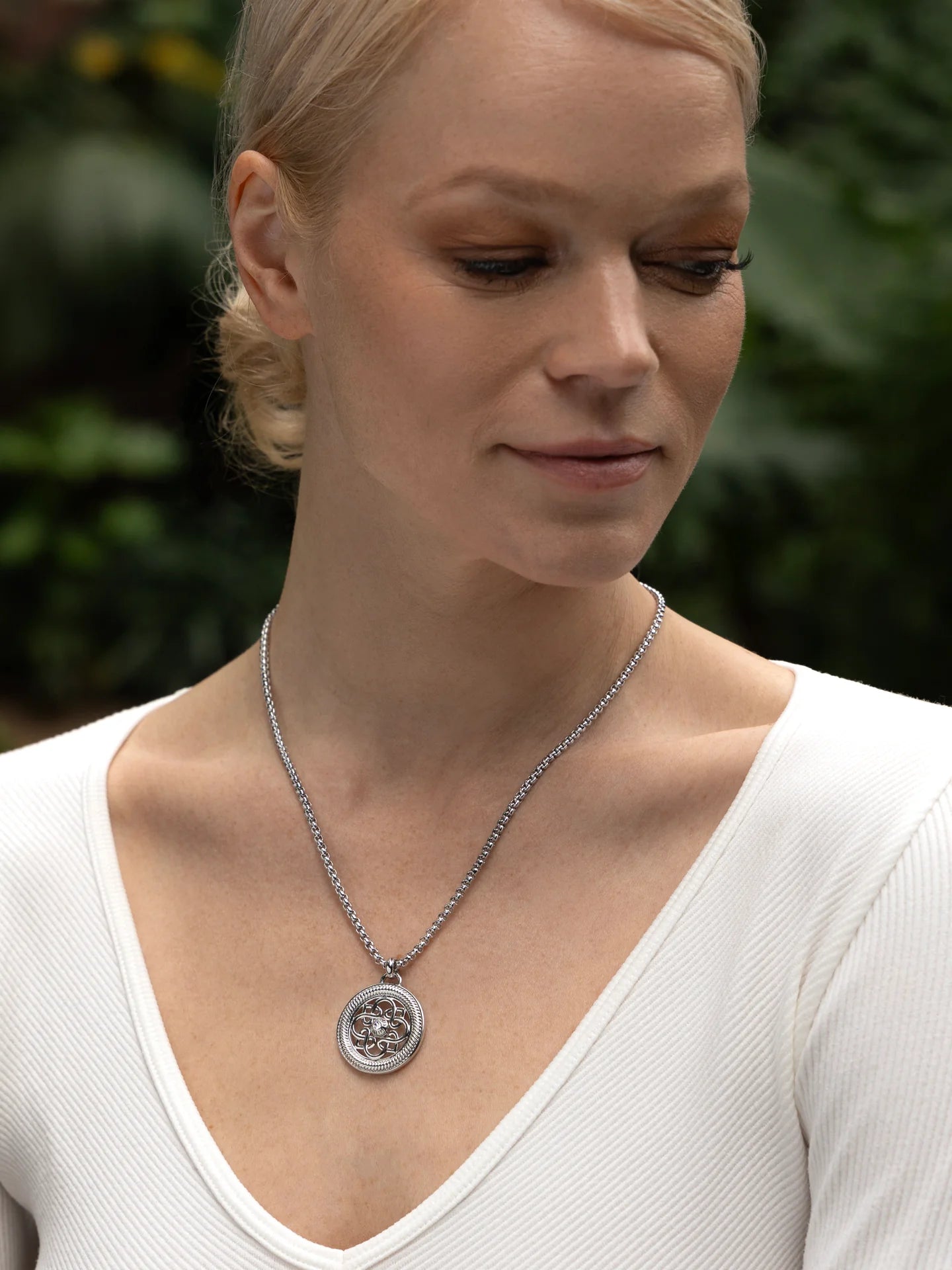 Woman wearing a white V-neck top and a silver pendant necklace outdoors
