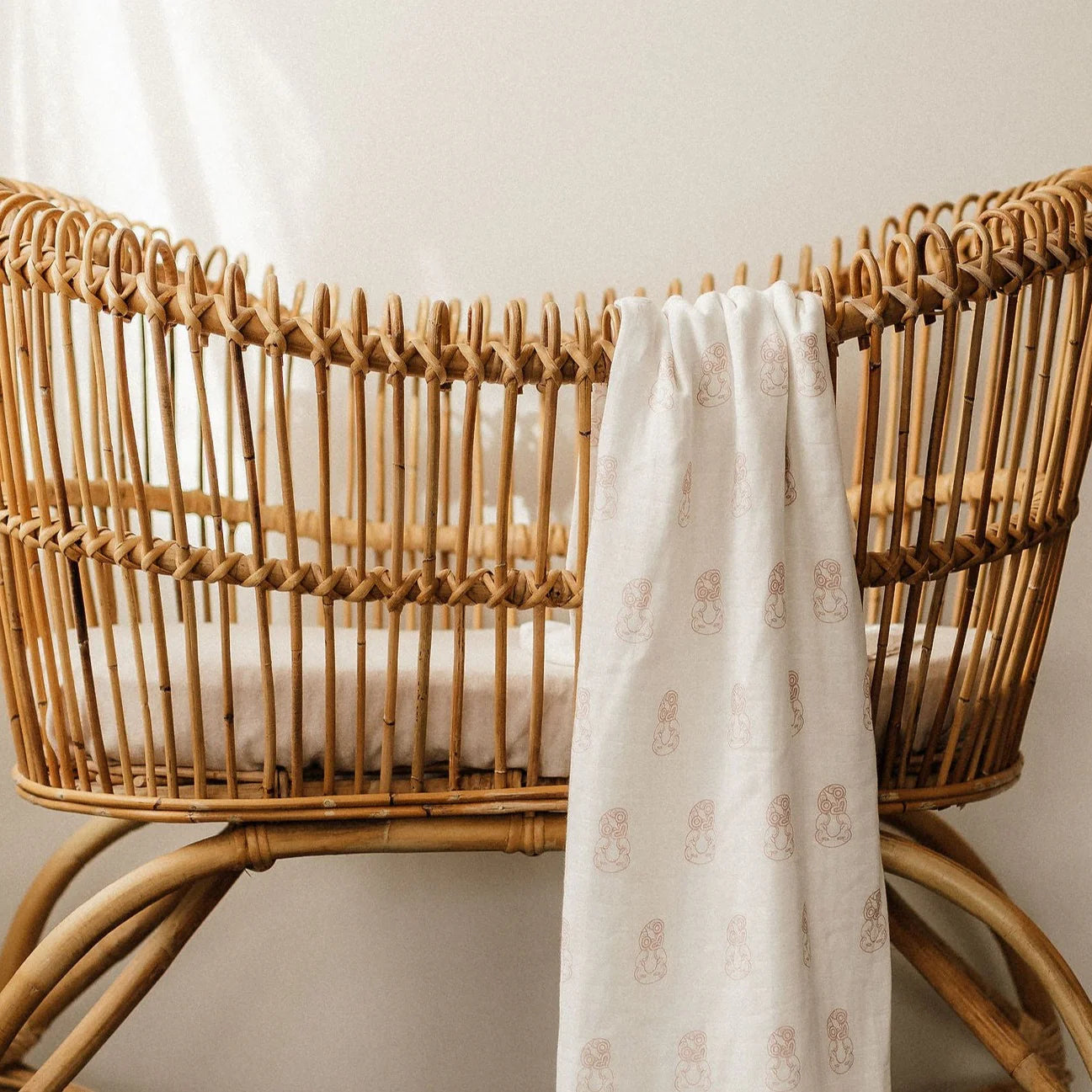 Natural rattan baby bassinet with a patterned linen blanket draped over the side