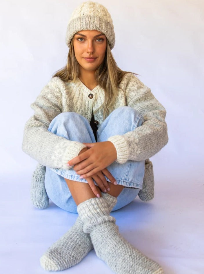 Woman wearing cozy knit hat, sweater, and socks, paired with light blue jeans, sitting casually