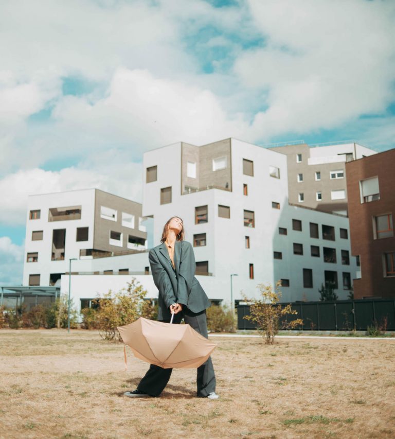 Woman in stylish outfit holding a beige mini umbrella outdoors near modern buildings