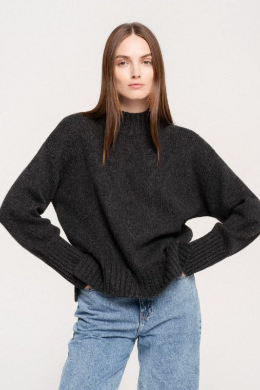 Woman wearing charcoal high neck sweater with high rib collar and cuffs.