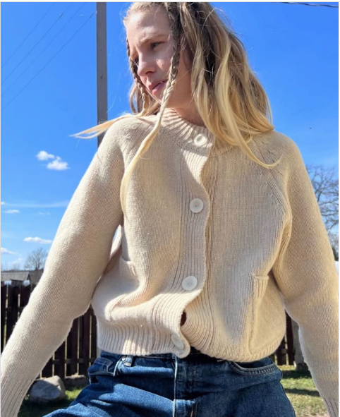 Woman wearing cream cashmere/merino cardigan with large buttons and front pockets.