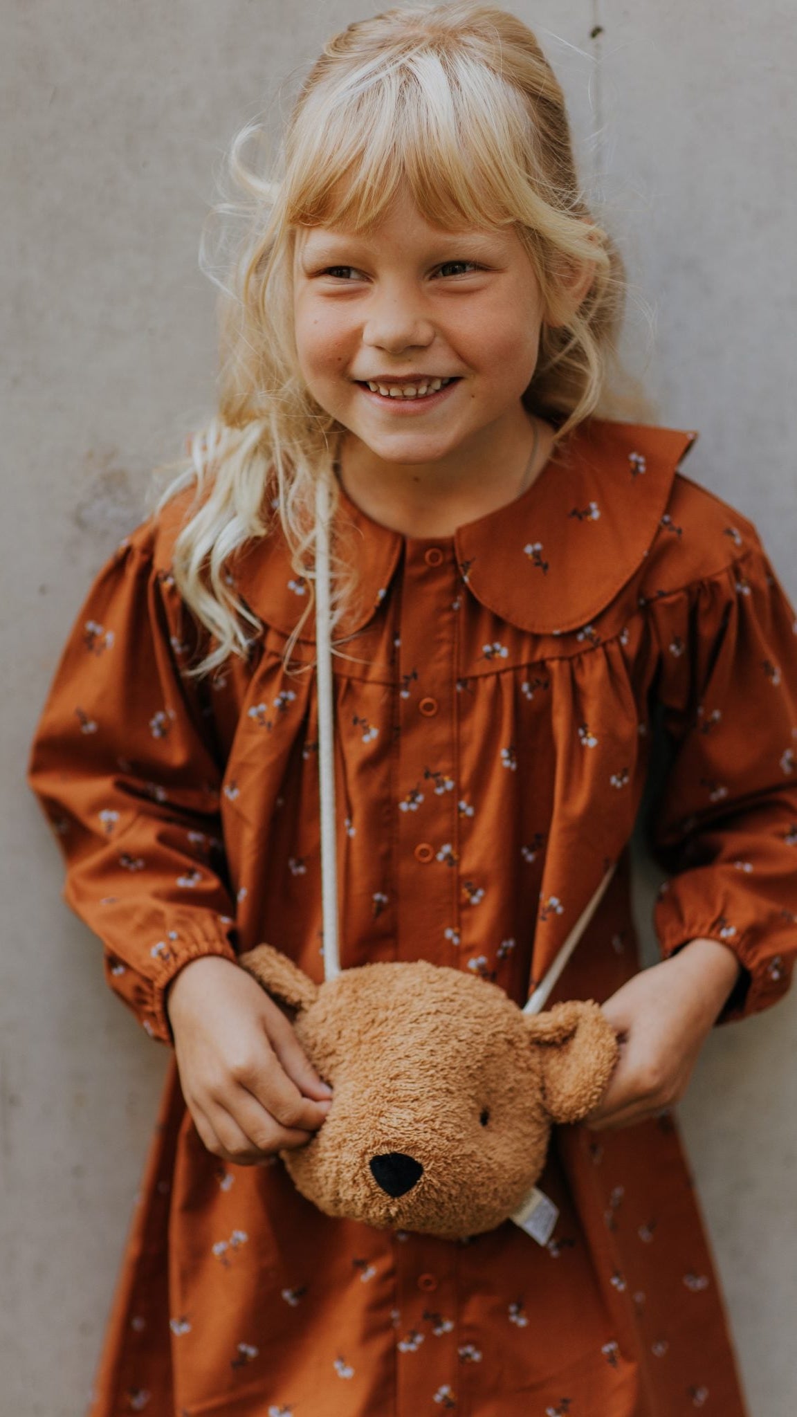 Child wearing teddy bag with long shoulder strap.