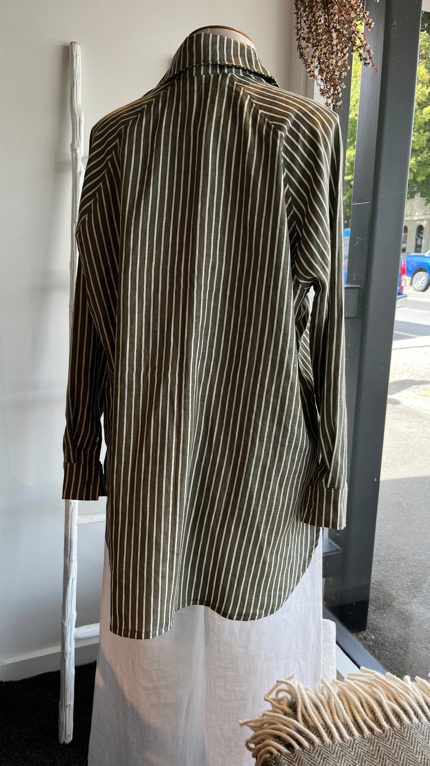 Back view of a green and white striped long sleeve linen shirt displayed on mannequin