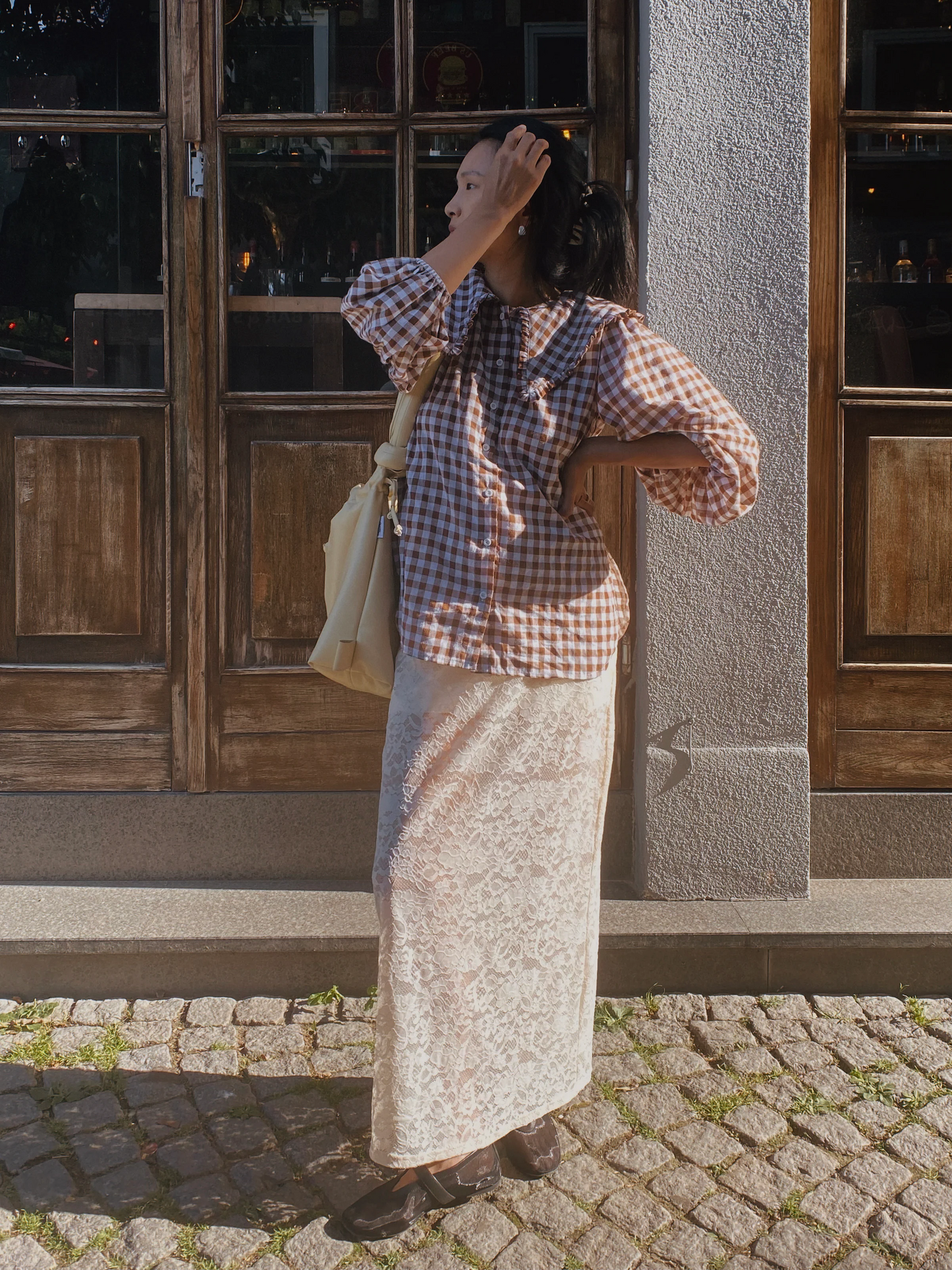 Woman wearing brown gingham blouse and cream lace skirt outdoors, stylish linen outfit