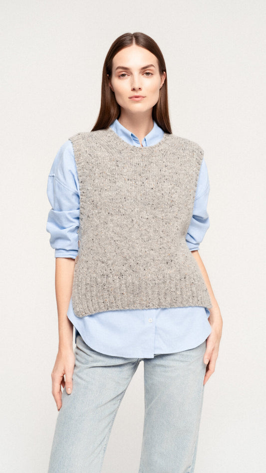 Woman wearing a grey knitted vest over a light blue shirt with light wash jeans