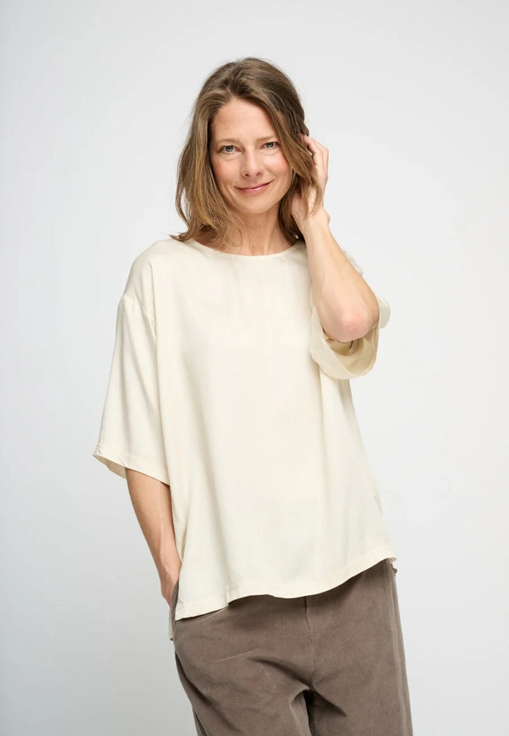Woman wearing cream silky satin short sleeve top with round neck.