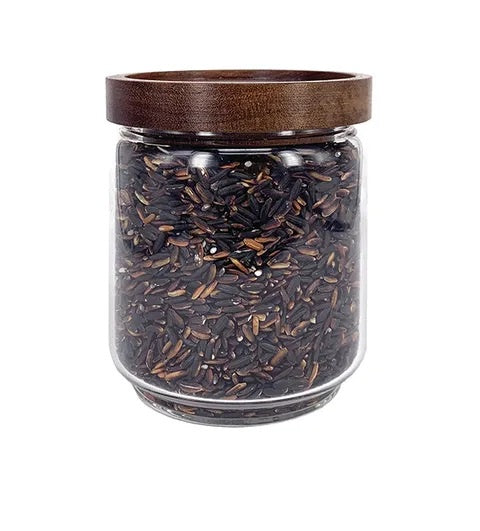 Glass jar with dark wild rice and wooden lid on white background