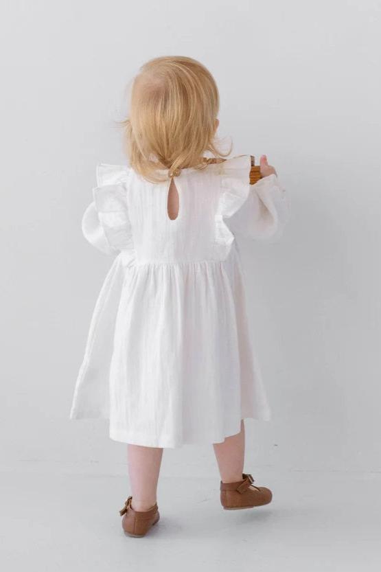 Back view of a toddler in a white linen dress with ruffle sleeves and tan shoes