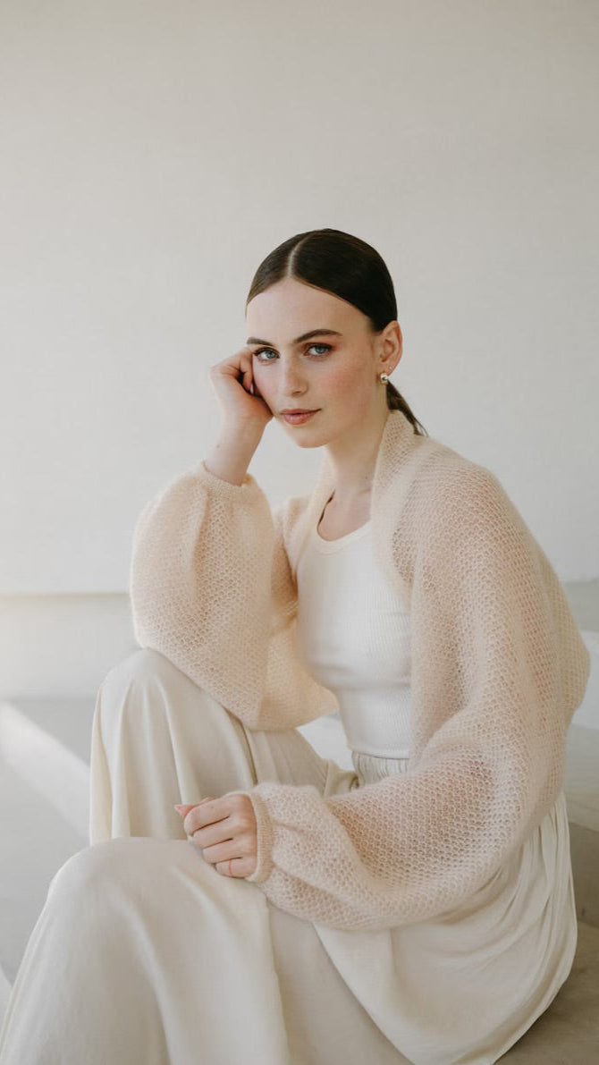 Woman sitting wearing fine knit mohair bolero with long puffed sleeve.