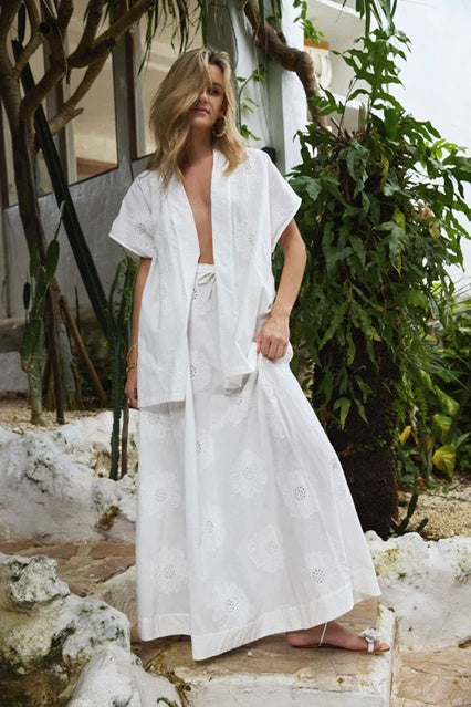 Woman wearing white linen skirt and shirt with floral embroidery, standing outdoors