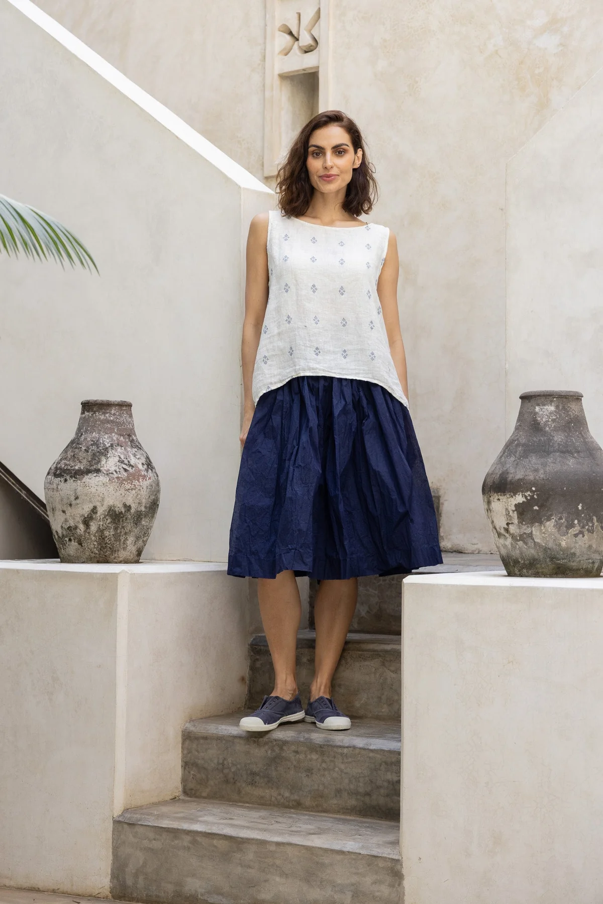Woman wearing a navy linen skirt and sleeveless white linen top in a minimalist setting