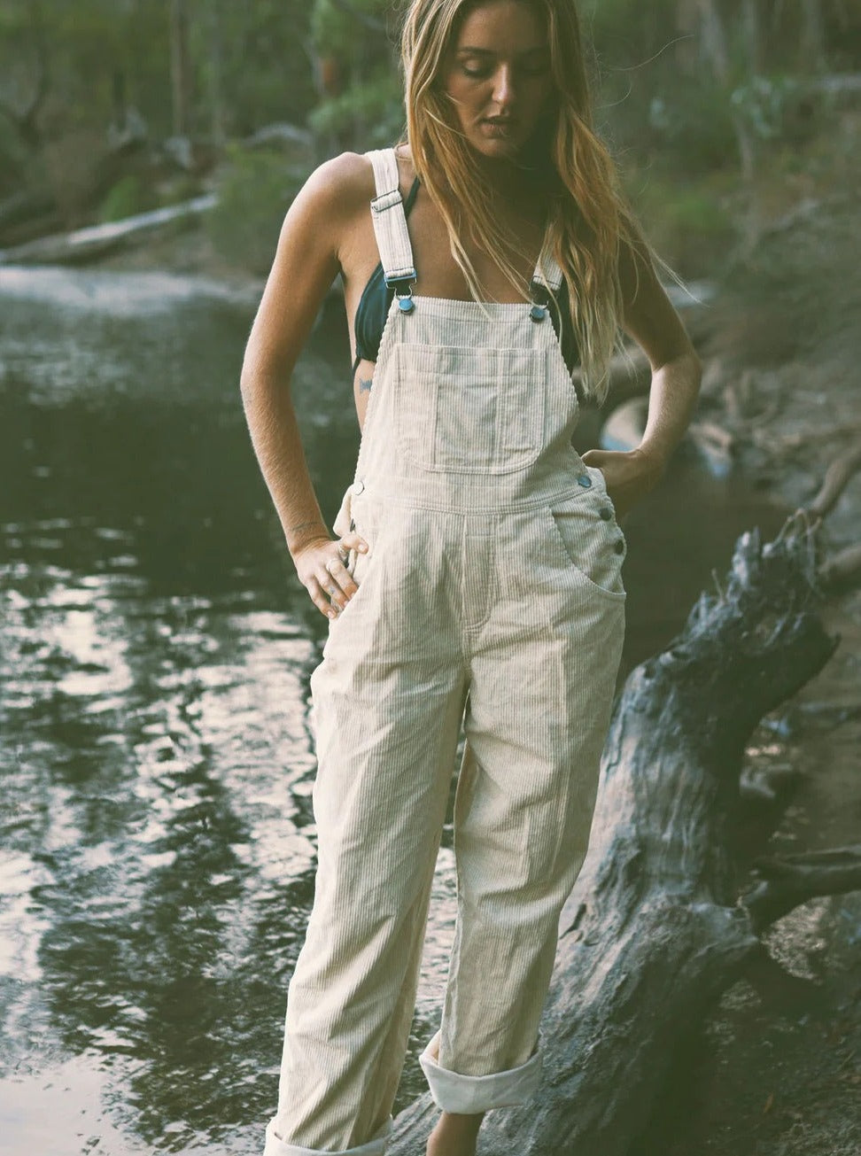 Woman wearing cream linen overalls by a riverside, casual outdoor fashion style