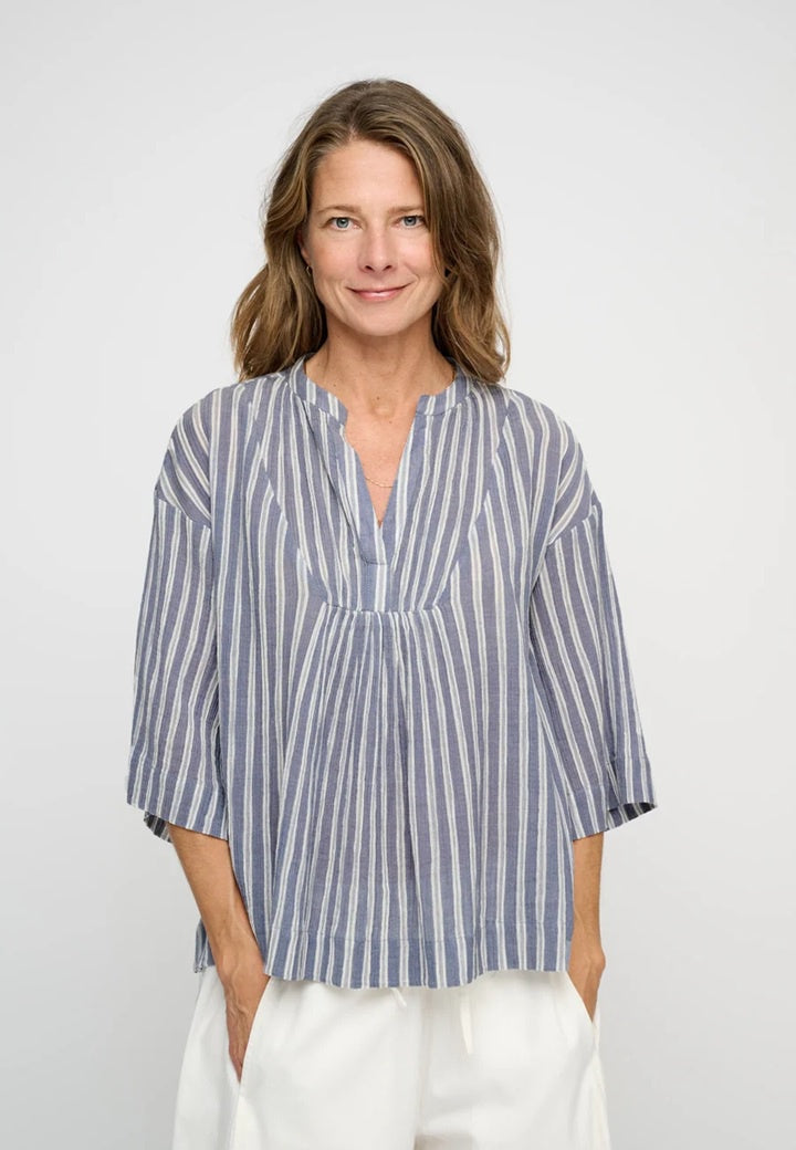 Woman wearing blue & white stripe organic cotton top with v neck and voluminous mid length sleeve.