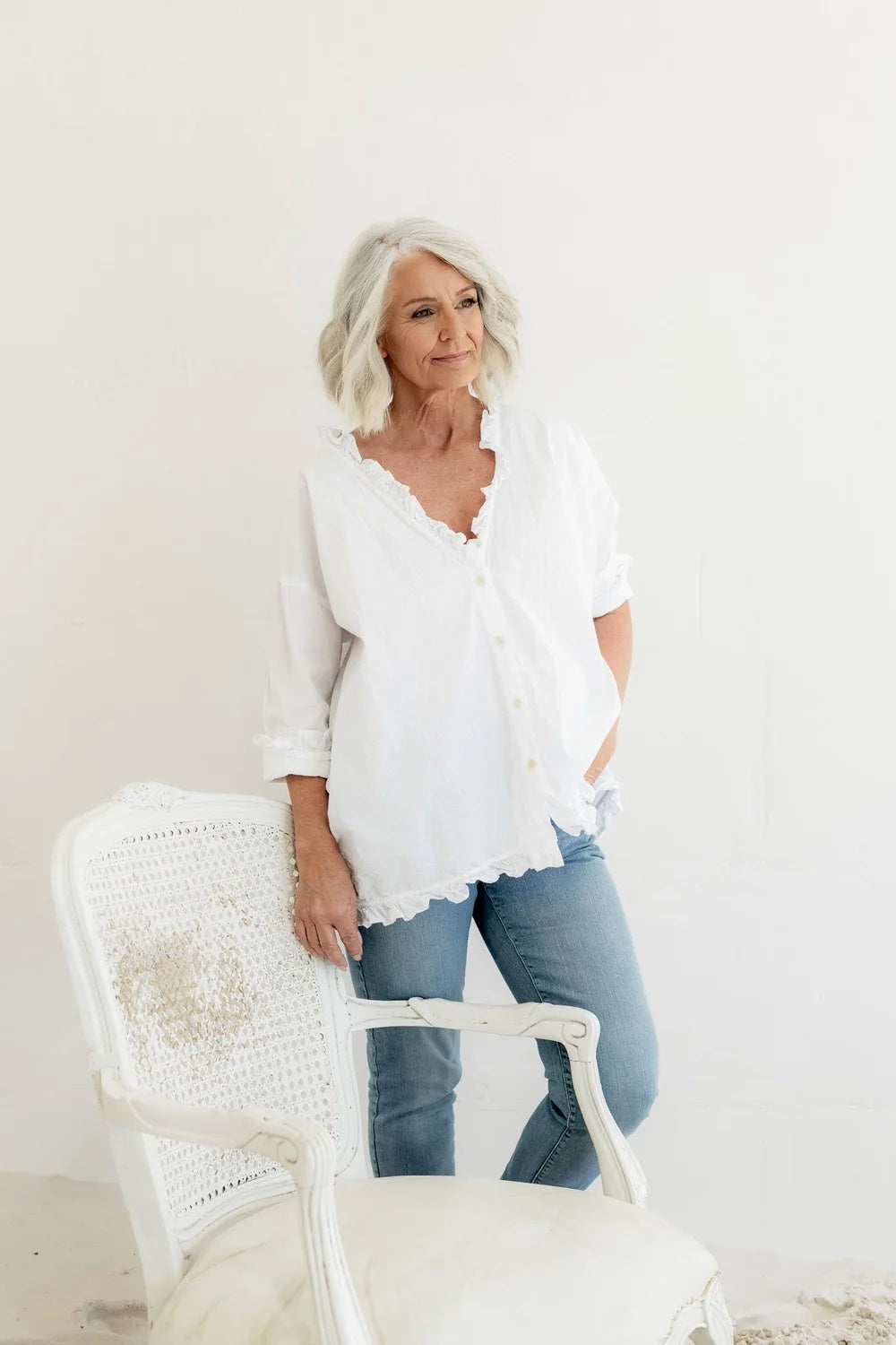Woman wearing a relaxed button through white shirt in cotton poplin with frills around the neck, cuff and hem.