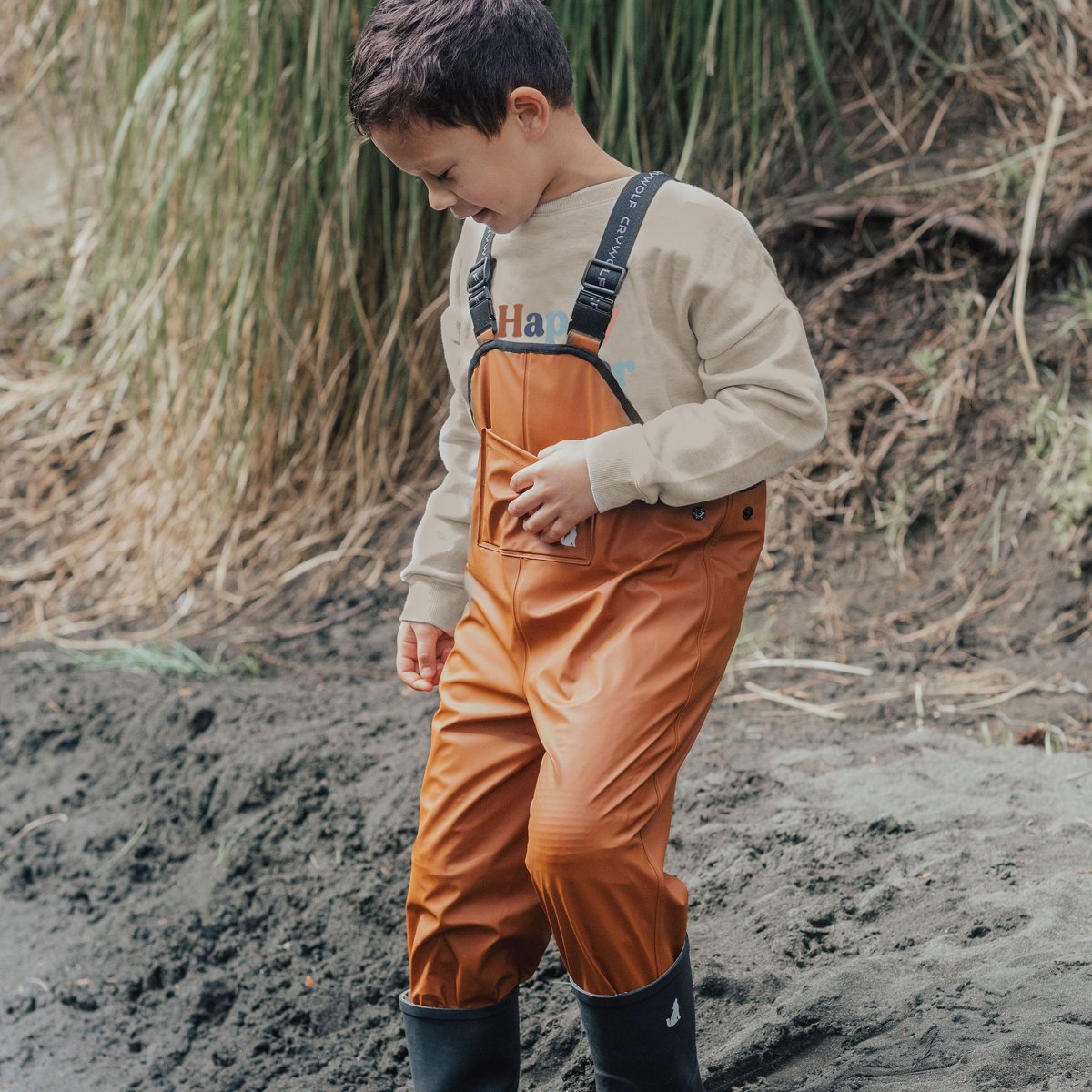 Happy kid playing outside wearing a crywolf overall in colour rust/clay