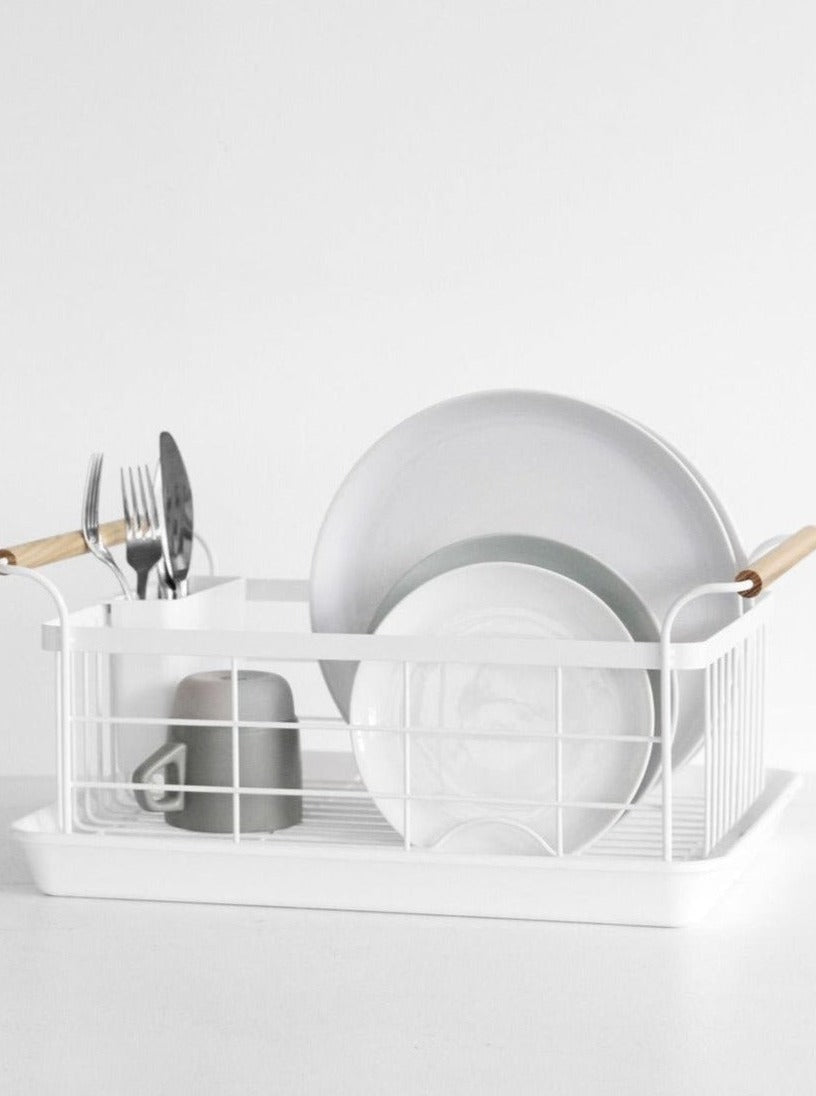 White dish rack with wooden handles holding plates, utensils, and a cup on a countertop