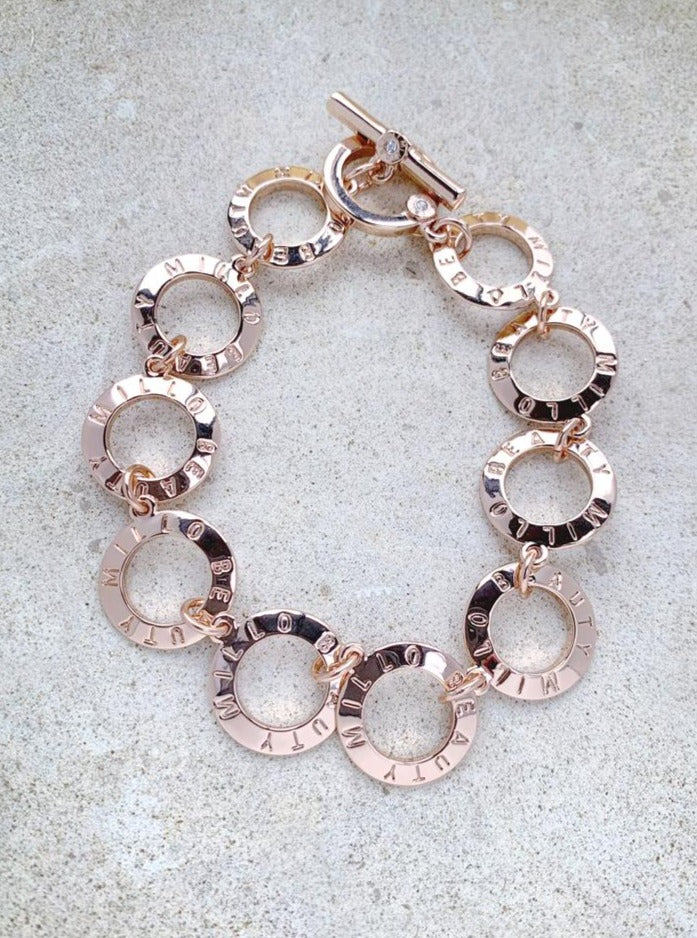 Rose gold circle link bracelet with engraved letters, on a neutral stone background