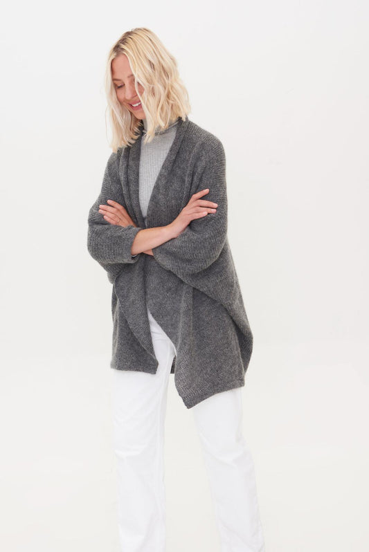Woman wearing a grey alpaca poncho over a light turtleneck and white pants