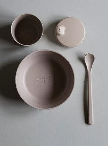 Neutral-toned dining set with bowl, cup, lid, and spoon on a light background