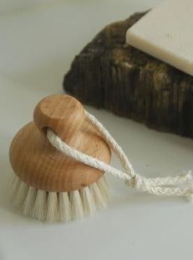 Wooden bath brush with natural bristles and cotton rope, next to soap and a dark stone tray.