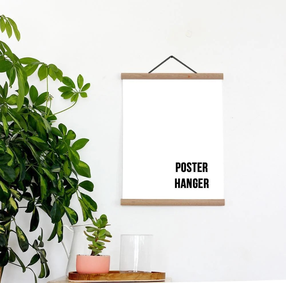 Wooden poster hanger displaying blank white paper on a wall with potted plants nearby