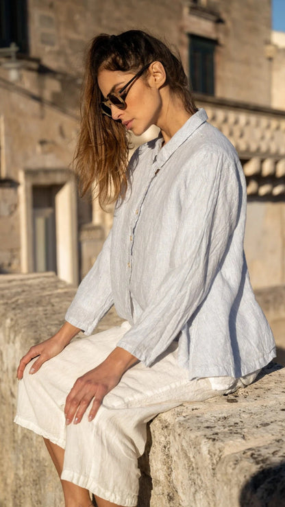 Woman wearing a light blue linen shirt and white linen pants outdoors in sunlight