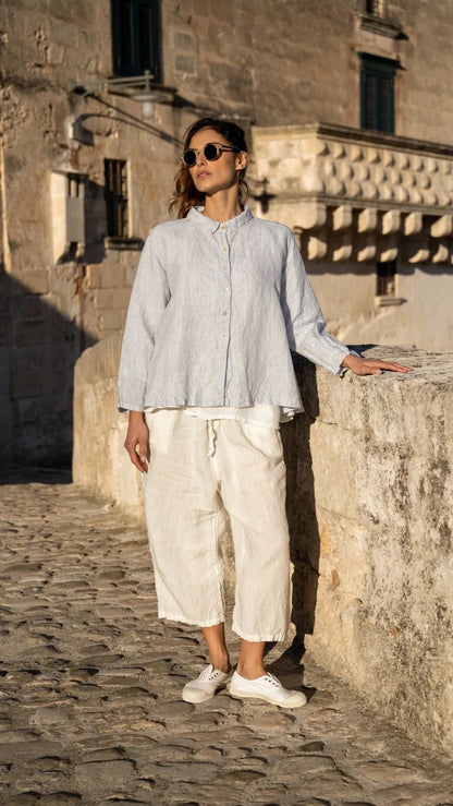 Woman wearing light blue linen shirt and white linen pants outdoors on stone walkway