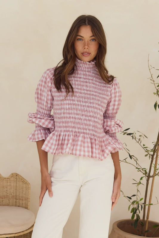 Woman wearing a blush gingham top with shirred bodice and frilled peplum.
