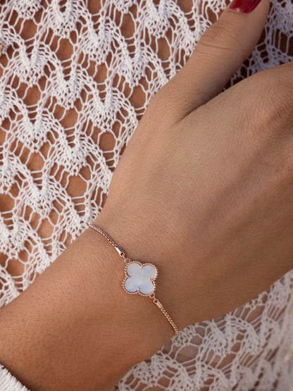 Delicate gold bracelet with white clover charm on wrist, worn over white lace top