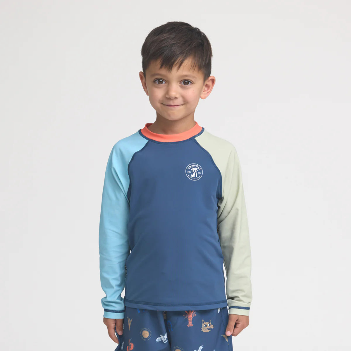 Smiling boy wearing colorblock long sleeve blue rash guard and printed swim shorts