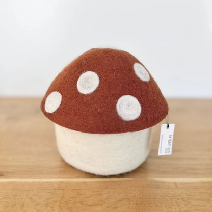 Felted mushroom ornament with brown cap and white spots on wooden surface