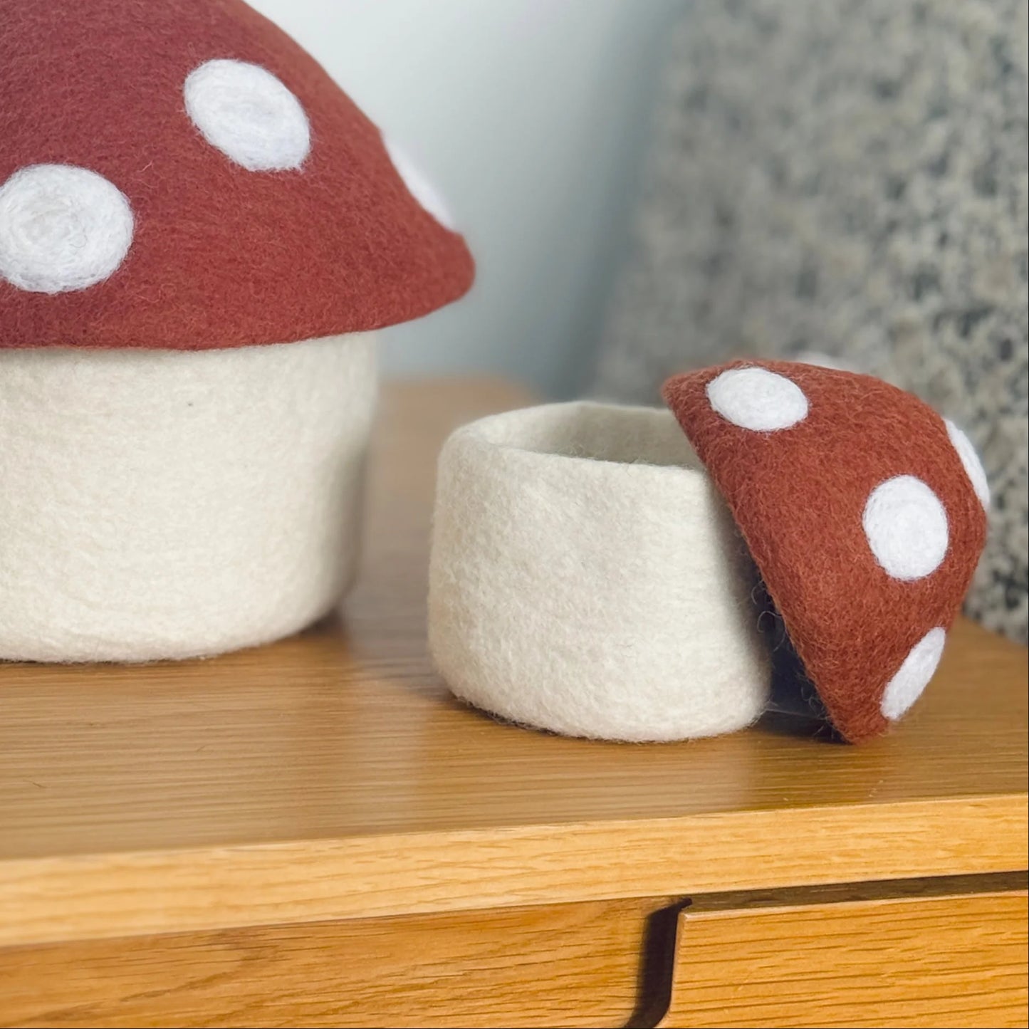 Felt mushroom-shaped storage containers with red tops and white polka dots on a wooden surface