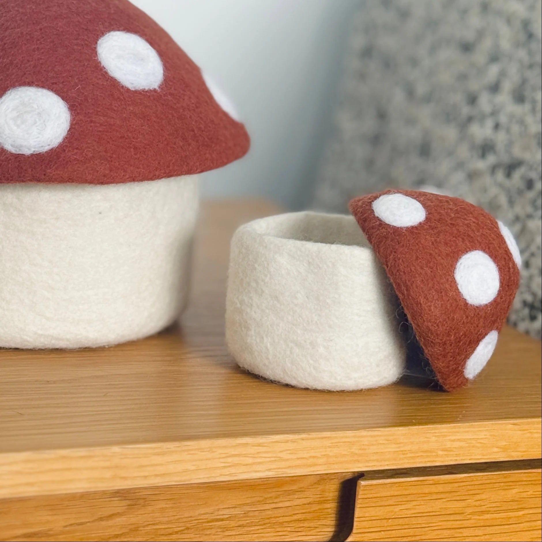 Felt mushroom-shaped storage containers with red tops and white polka dots on a wooden surface