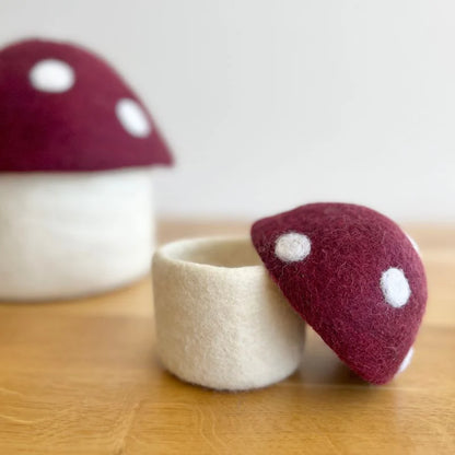 Felt mushroom-shaped container with white stem and red cap with white spots on wood surface