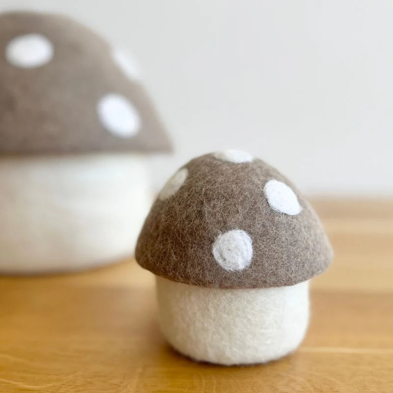 Decorative felt mushroom ornament with brown and white polka dot cap on wooden surface