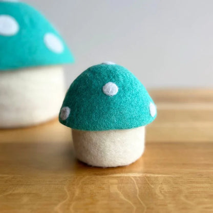 Handmade felt mushroom ornament with teal and white cap on wooden surface