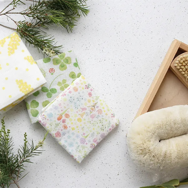 Floral and clover patterned linen cloths on a white surface with a natural cleaning brush
