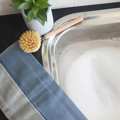 Blue linen tea towel beside kitchen sink with dish brush and green plant on countertop