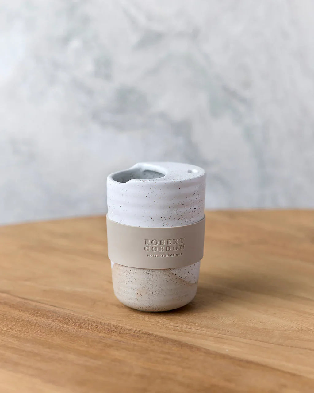Speckled ceramic reusable coffee cup with silicone band on wooden table