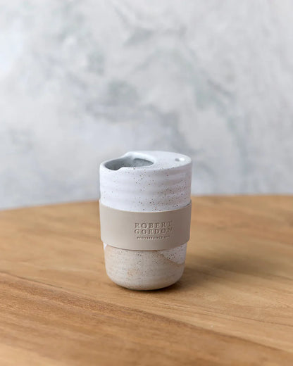 Speckled ceramic reusable coffee cup with silicone band on wooden table