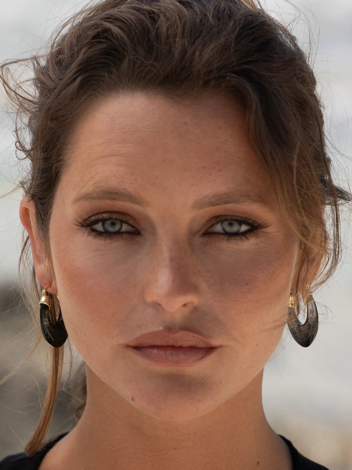 Closeup of woman wearing black hoop earrings and natural makeup, outdoor setting