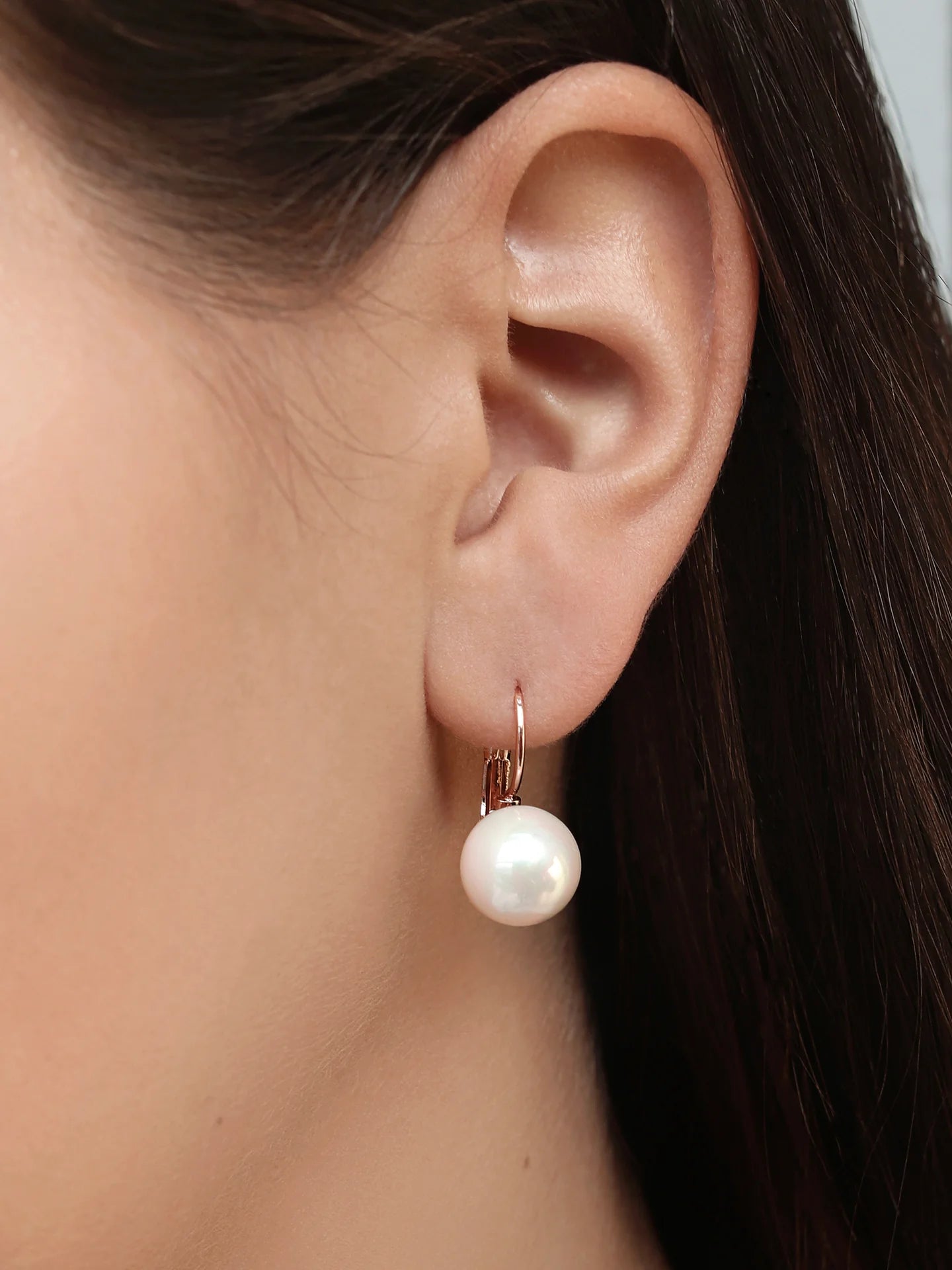 Woman wearing a gold hoop earring with a large white pearl drop