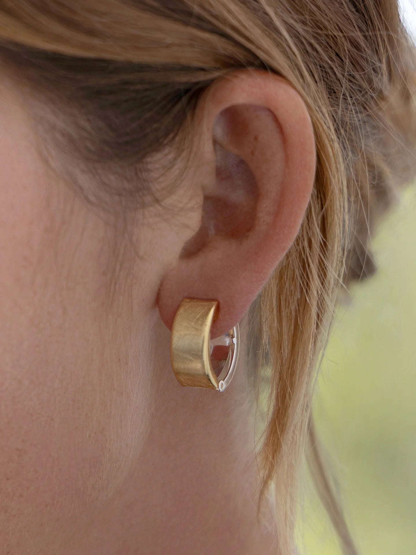 Close-up of a woman wearing a wide gold hoop earring