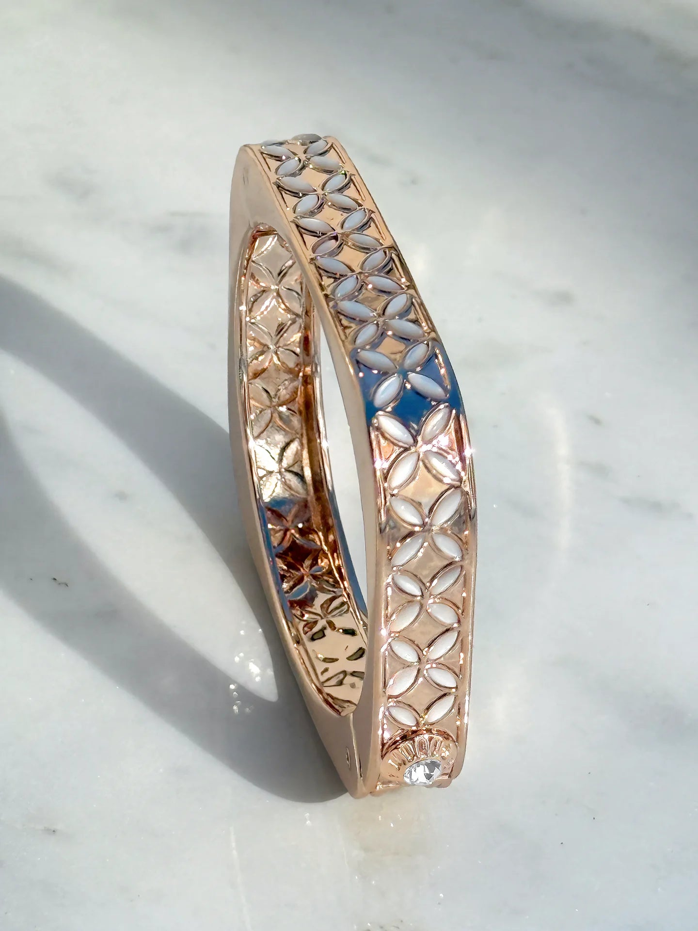 Rose gold bangle with lattice pattern and white accents, placed on a marble surface