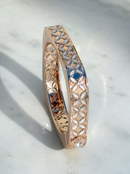 Rose gold bangle with lattice pattern and white accents, placed on a marble surface