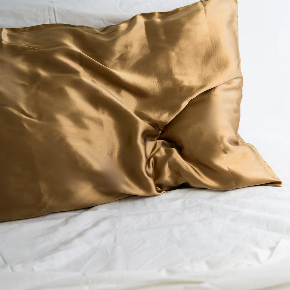 Gold silk pillowcase on white linen bedding, luxury bedroom decor