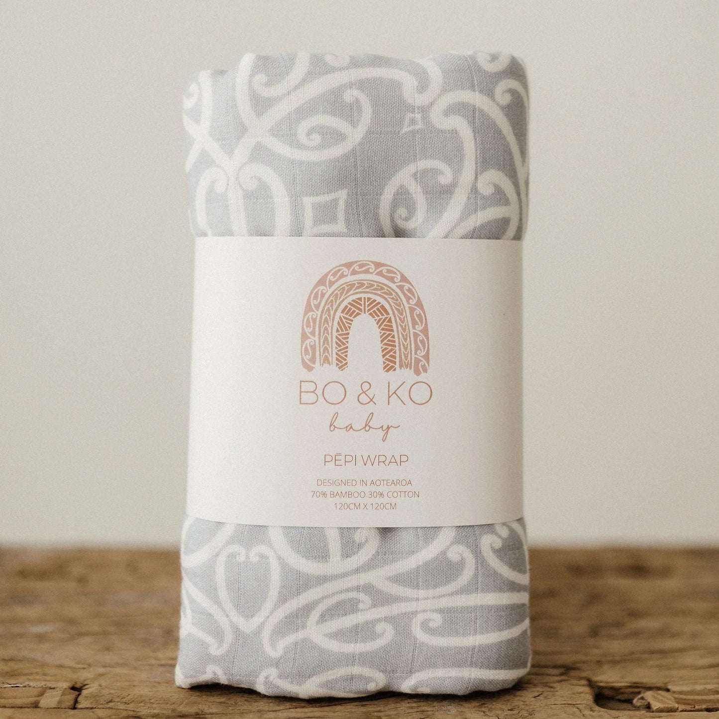 Grey and white patterned baby wrap with Bo & Ko Baby label, on wooden surface