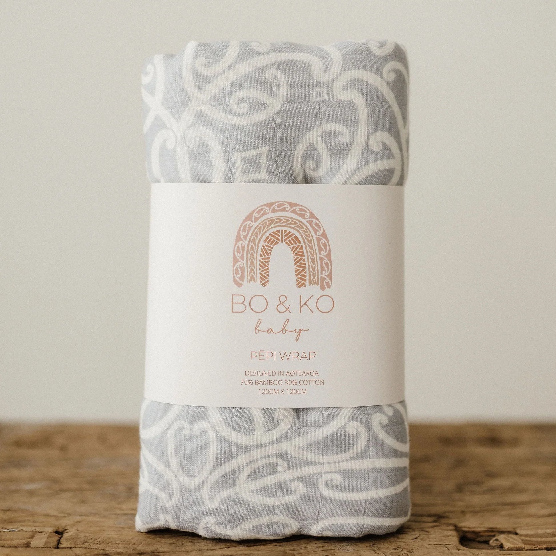 Grey and white patterned baby wrap with Bo & Ko Baby label, on wooden surface